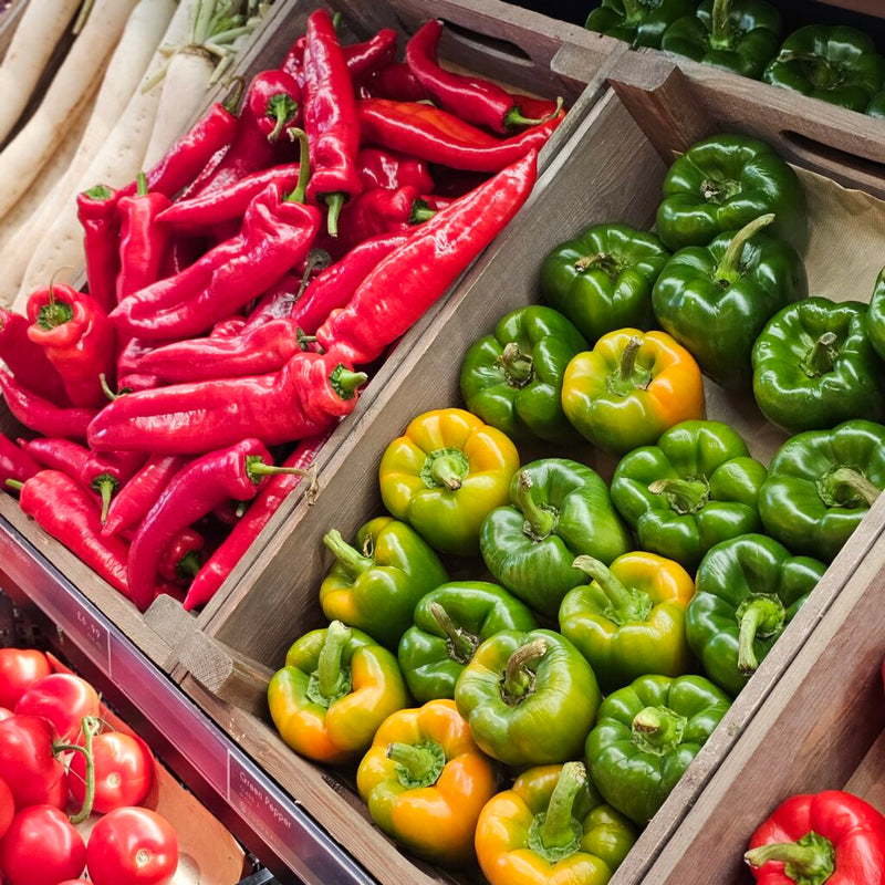 Wooden crates filled with red, green, and yellow bell peppers.